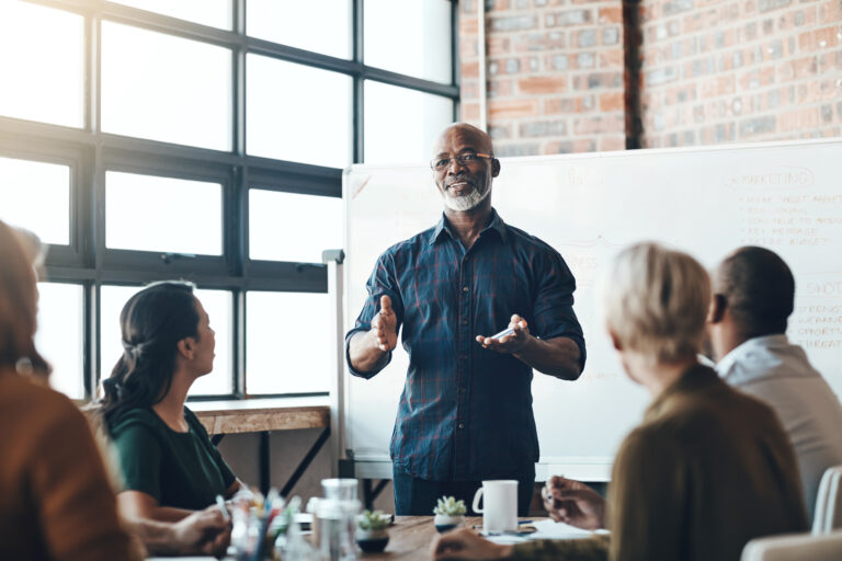 Senior business man doing presentation, planning and talking in a meeting, seminar or training workshop in a boardroom. Manager sharing ideas, teaching and coaching new employees during conference.